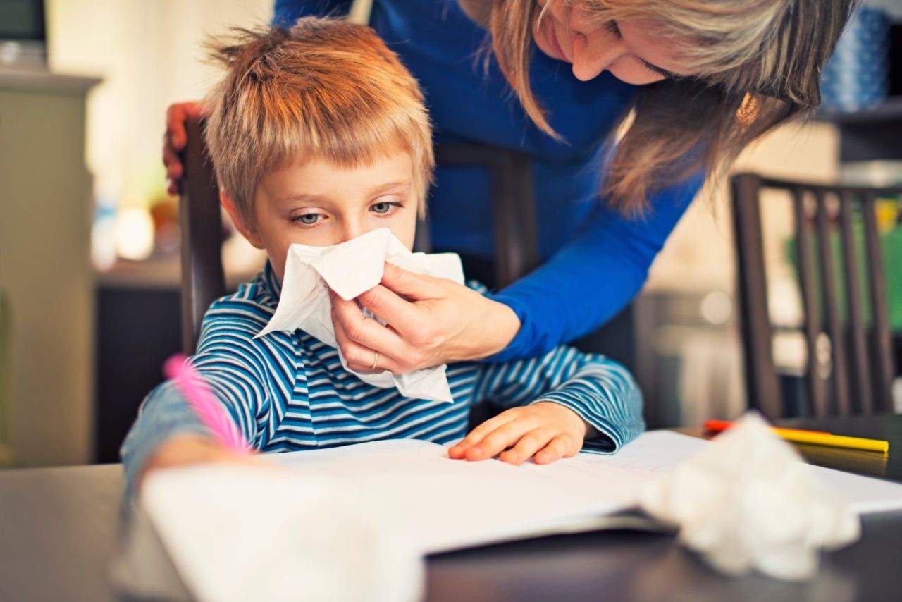 Mother helping child wipe nose during homework time, illustrating family health and hygiene care