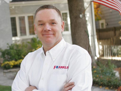 Franklin tech standing outside a house in branded uniform with arms crossed