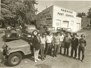 A group of men standing in front of a building, seemingly discussing ways to manage local rodents.
