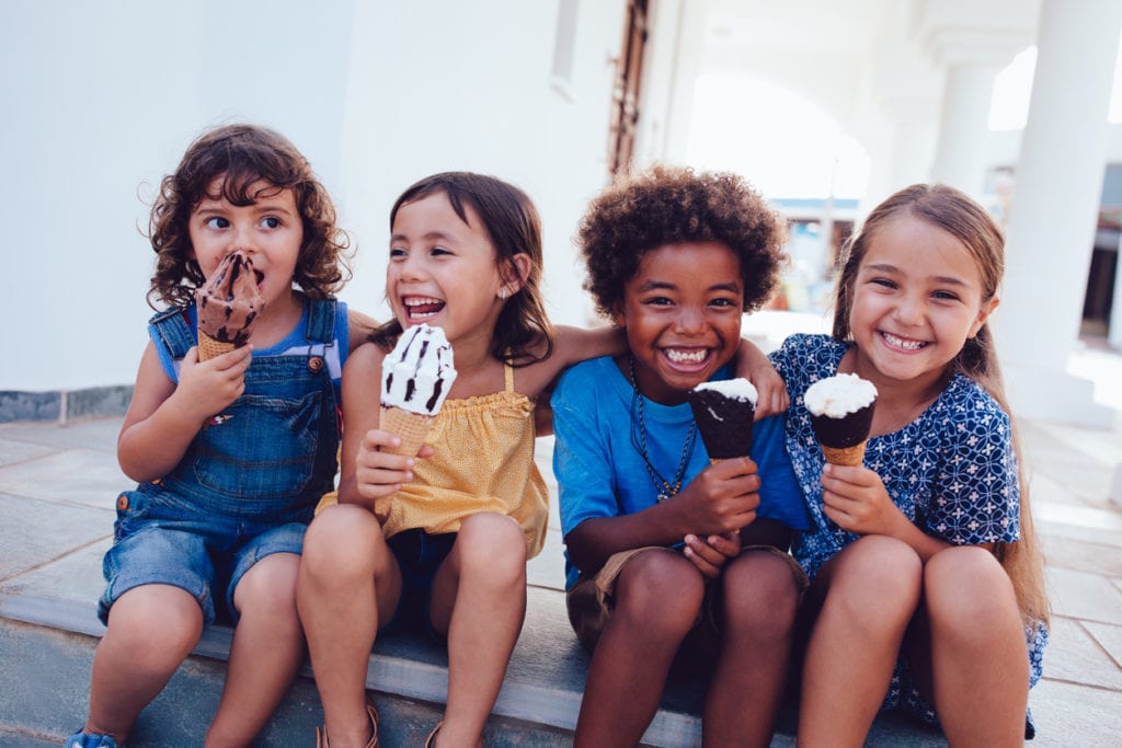 Four children sit on steps outside, smiling and holding ice cream cones, enjoying their treat while learning how to keep wasps away.