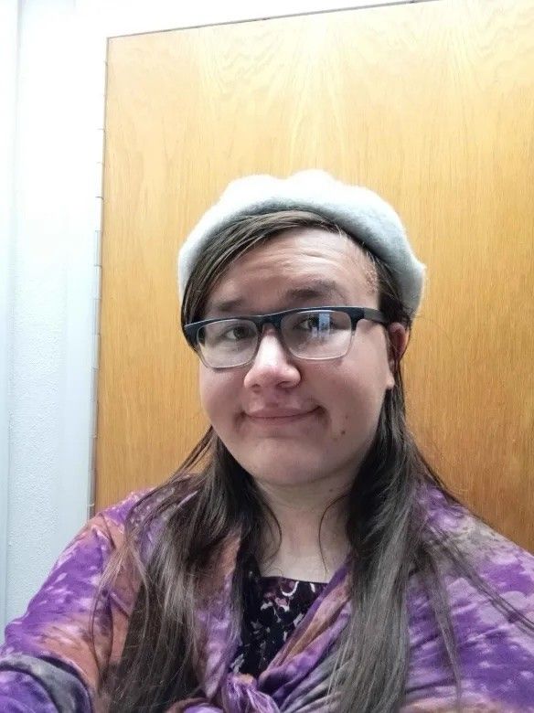 Aster Barajas wearing glasses and a light beret, portrait-style photo indoors